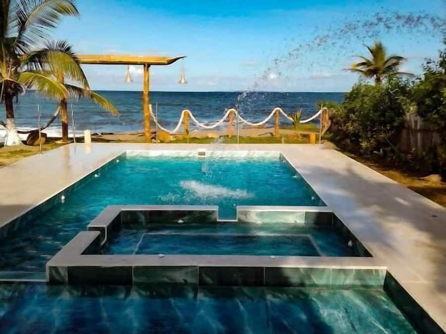 Una piscina con vista al océano, rodeada de palmeras y una pérgola de madera.