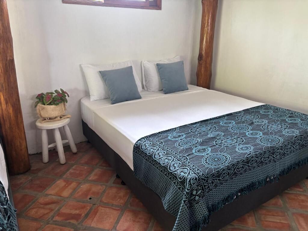 A bed with a patterned bedspread, a small stool with a plant, and a window above the bed.