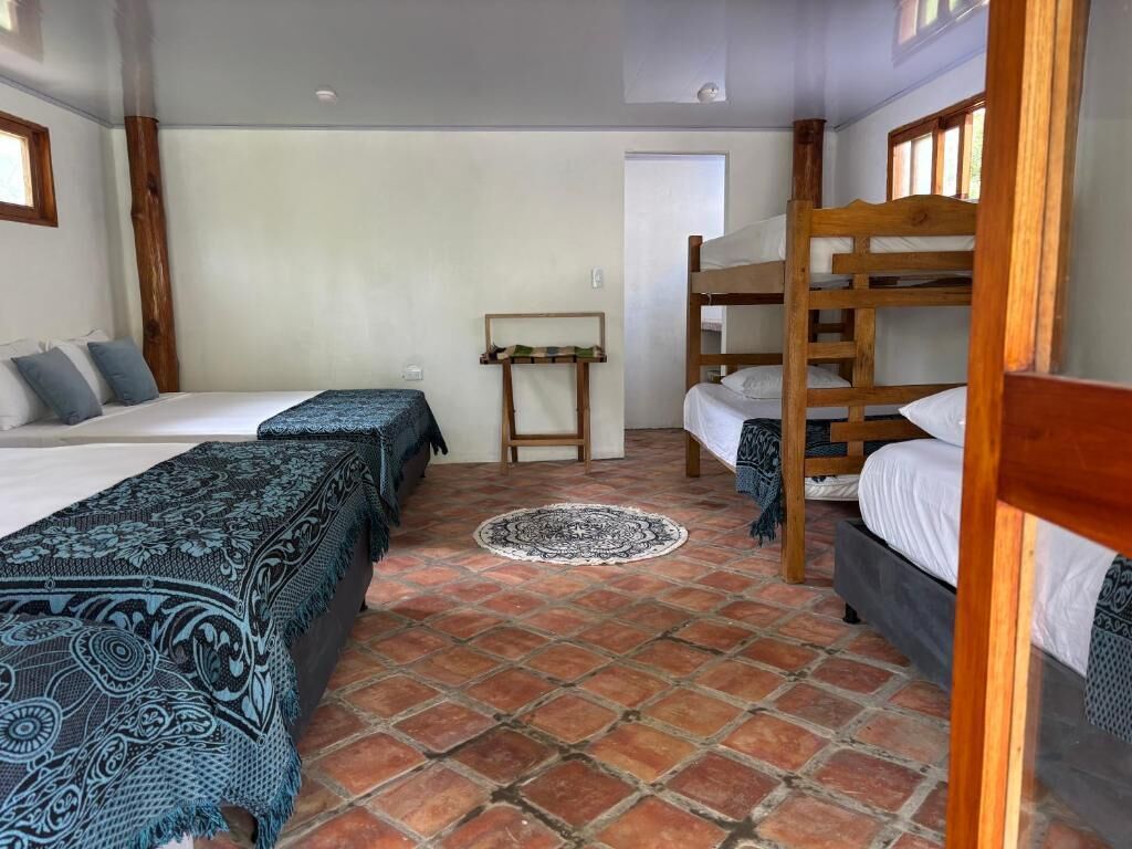 A room with two beds, a wooden bunk bed, a patterned rug, and a door in the background.