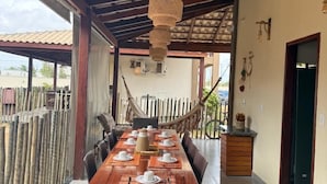 Un espace repas avec une longue table en bois, des chaises en osier et un hamac.