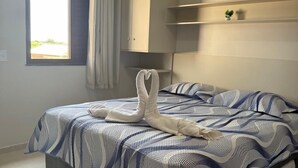 Une chambre à coucher avec un lit, une fenêtre, un radiateur et une étagère sur laquelle se trouve une plante.