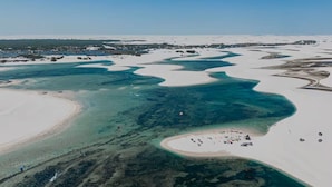 Vue aérienne d’une zone côtière avec des canaux aux eaux claires, des plages de sable et quelques bâtiments dispersés.