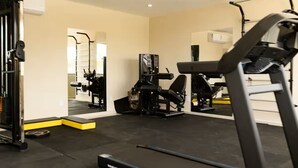 Une salle de sport équipée de matériel d’exercice, d’un tapis de course et d’un mur recouvert de miroirs.