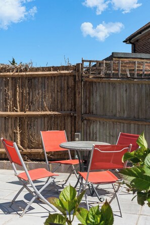 A patio with a table and four chairs, a wooden fence, and a building in the background. - FREE Driveway | Sleeps 12 | 4 BR Detached | Near AMEX | Garden (Brighton and Hove)