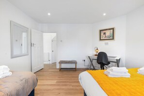 Une chambre avec deux lits, un bureau avec une chaise, un banc et un tableau au mur.