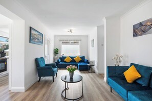 A modern living room with a blue sofa set, a round coffee table, and a dining area with a black table and chairs. - FREE Driveway | Sleeps 12 | 4 BR Detached | Near AMEX | Garden (Brighton and Hove)