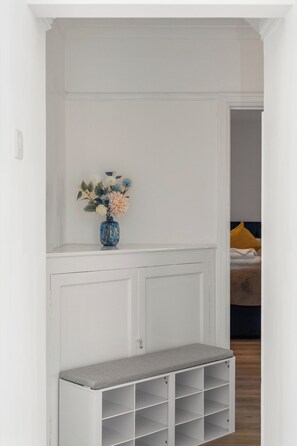A white room with a bench and a blue vase with flowers. - FREE Driveway | Sleeps 12 | 4 BR Detached | Near AMEX | Garden (Brighton and Hove)