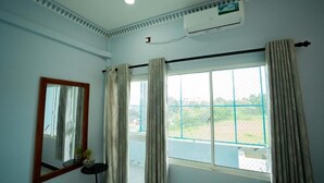 A room with a large window, a ceiling fan, and a wall-mounted air conditioner.