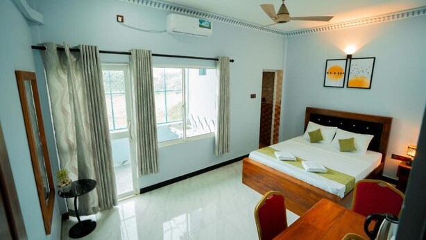 A hotel room with a bed, a desk, a chair, a ceiling fan, and a window with curtains.