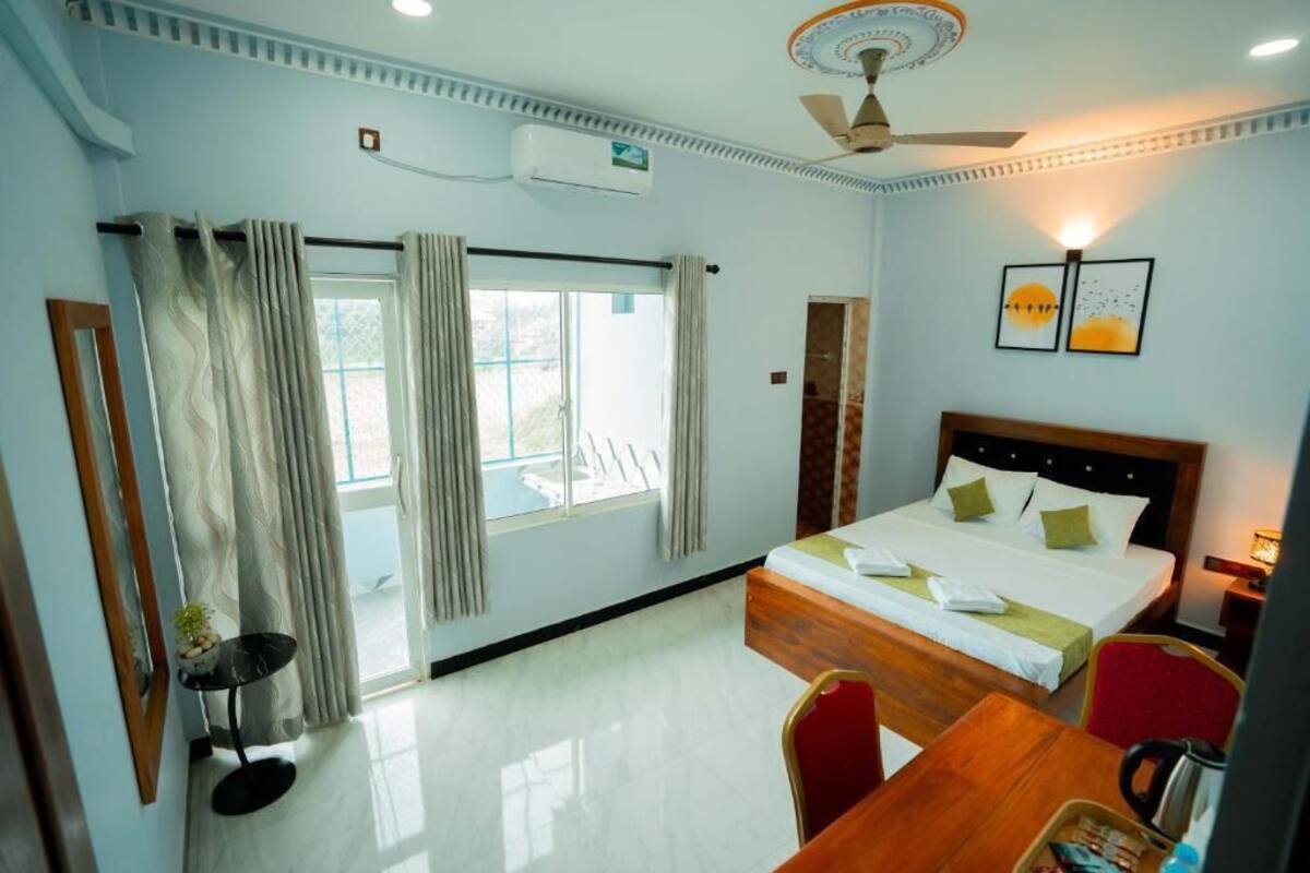 Ein Hotelzimmer mit Bett, Schreibtisch, Stuhl, Deckenventilator und einem fenster mit Vorhängen.