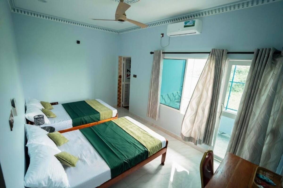 Ein Zimmer mit zwei Betten, einem Deckenventilator, einer Klimaanlage und einem Fenster mit Vorhängen.