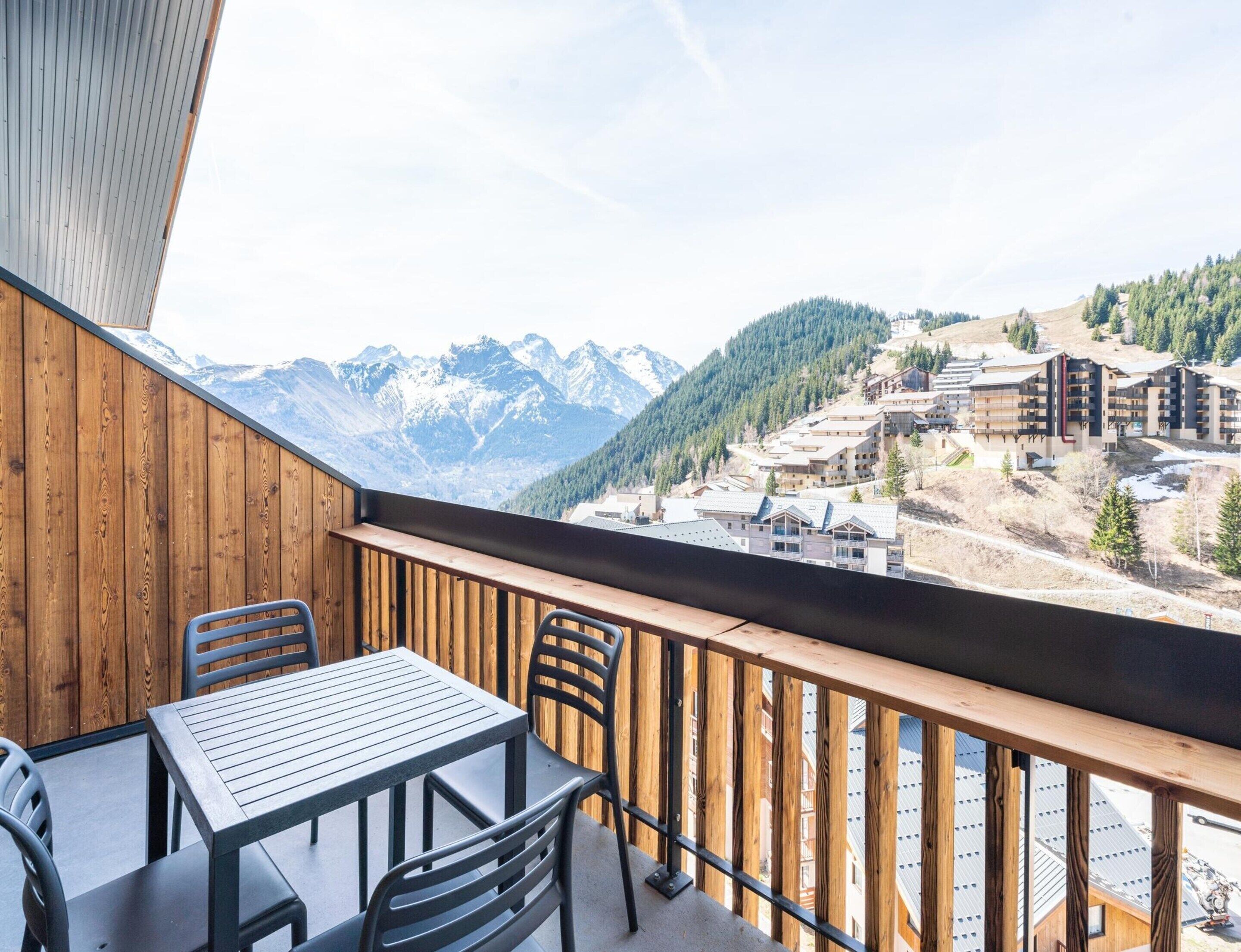 A balcony with a table and chairs, overlooking a mountainous landscape with buildings.