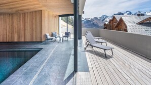 A modern outdoor pool area with wooden slats, lounge chairs, and a view of mountains. - Base With Ski-in/ski-out Access (Auris)