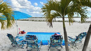 A beach with four lounge chairs and a blue umbrella. - Luxury Beachfront Condo with Seasonally Heated Beachside Pool (Fort Myers Beach)