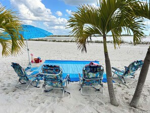Ein Strand mit vier Liegestühlen und einem blauen Sonnenschirm.