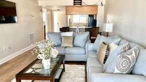 A living room with a sofa, a coffee table, and a TV. - Luxury Beachfront Condo with Seasonally Heated Beachside Pool (Fort Myers Beach)