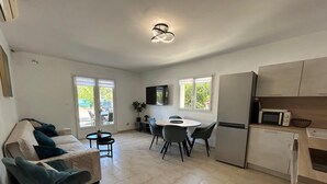 Ett kompakt bostadsutrymme med en soffa, ett matbord, stolar, en TV och ett köksområde som inkluderar en mikrovågsugn och ett kylskåp.