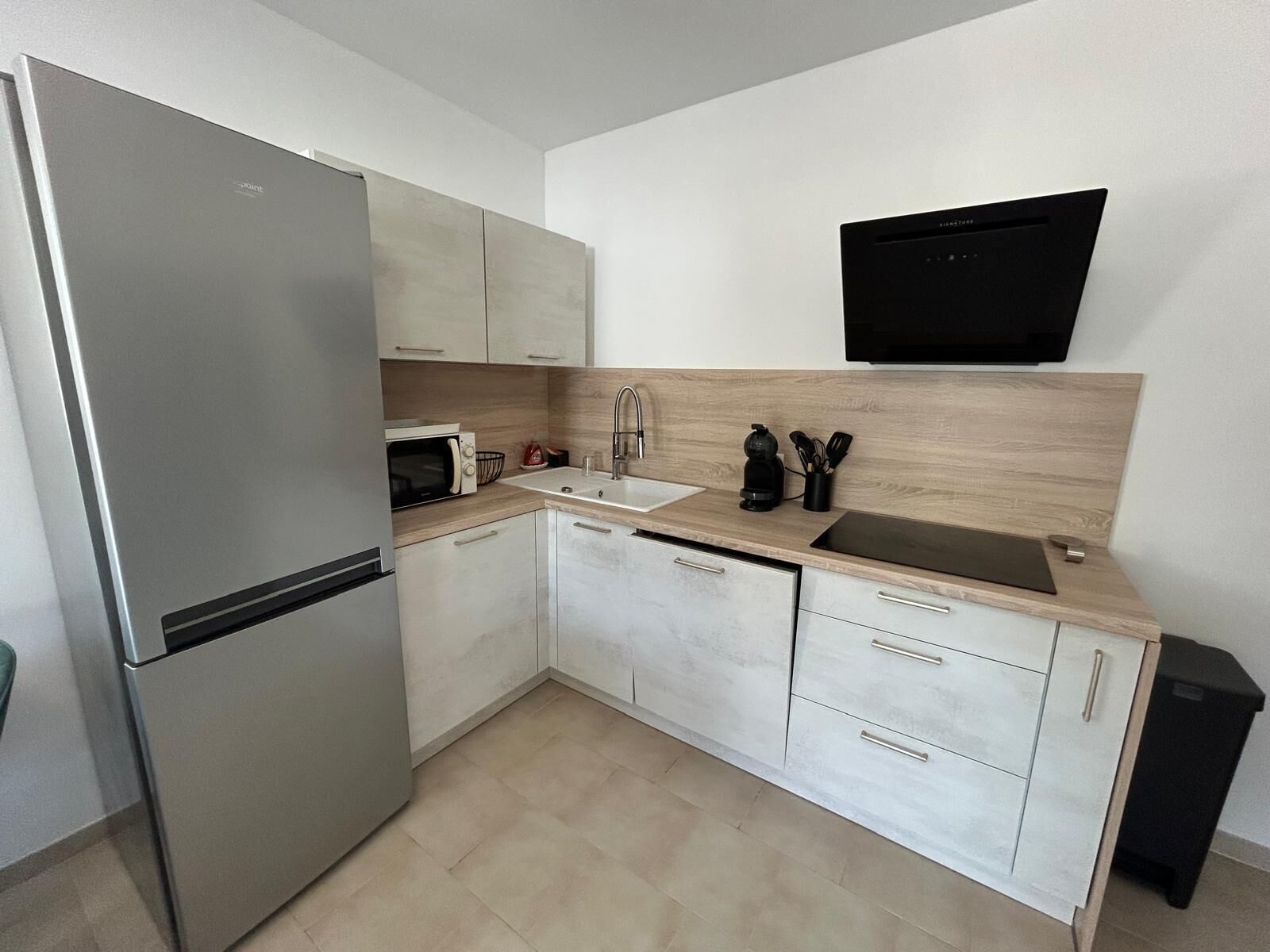 Eine moderne Küche mit einem Edelstahl-Kühlschrank, einer Mikrowelle, einer Spüle und einer schwarzen Dunstabzugshaube.