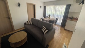 Una sala de estar con sofá, una mesa redonda, una mesa de comedor con sillas, una zona de cocina y una puerta.