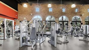 Ett gym med olika träningsmaskiner, stora fönster och en tegelvägg.
