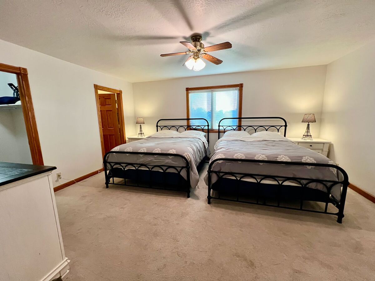 A bedroom with two beds, a ceiling fan, a window, and a nightstand with a lamp.
