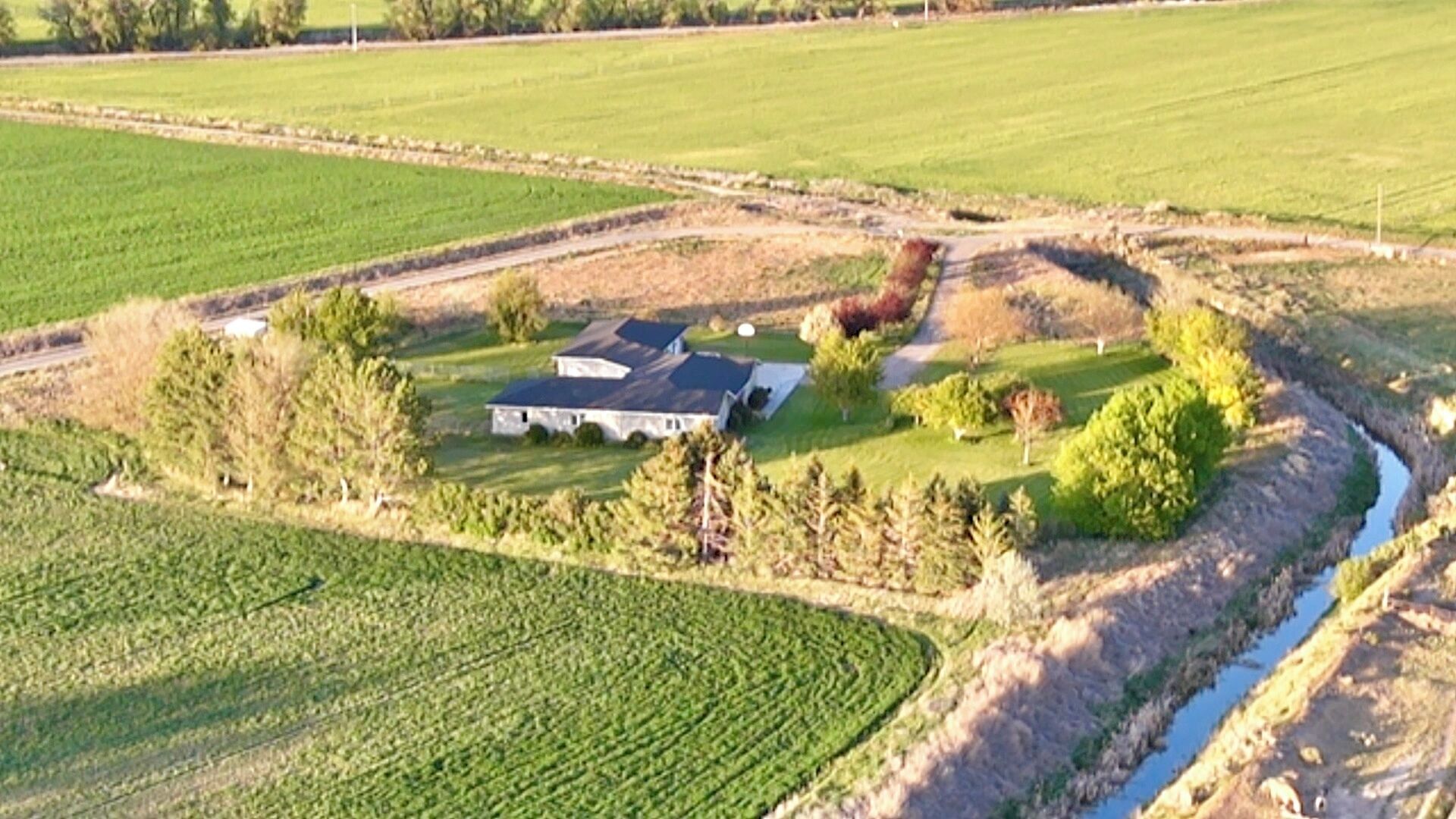 Ett flygbildsbild av en lantlig fastighet med ett stort hus, omgivande åkrar och en slingrande bäck.