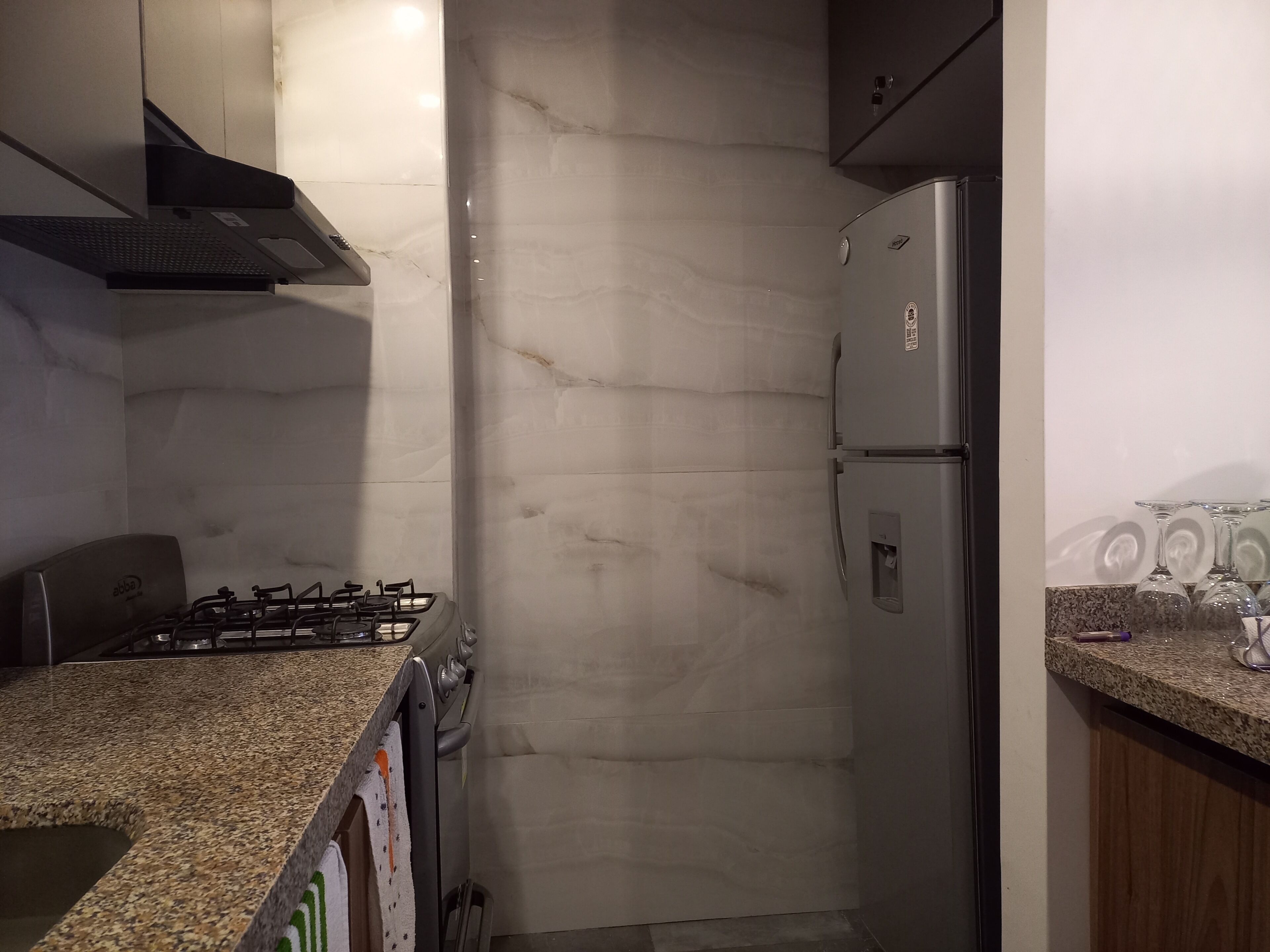 A kitchen with a gas stove, stainless steel refrigerator, granite countertop, and marble backsplash.