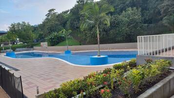 A swimming pool with a tiled deck, surrounded by plants and a fence.
