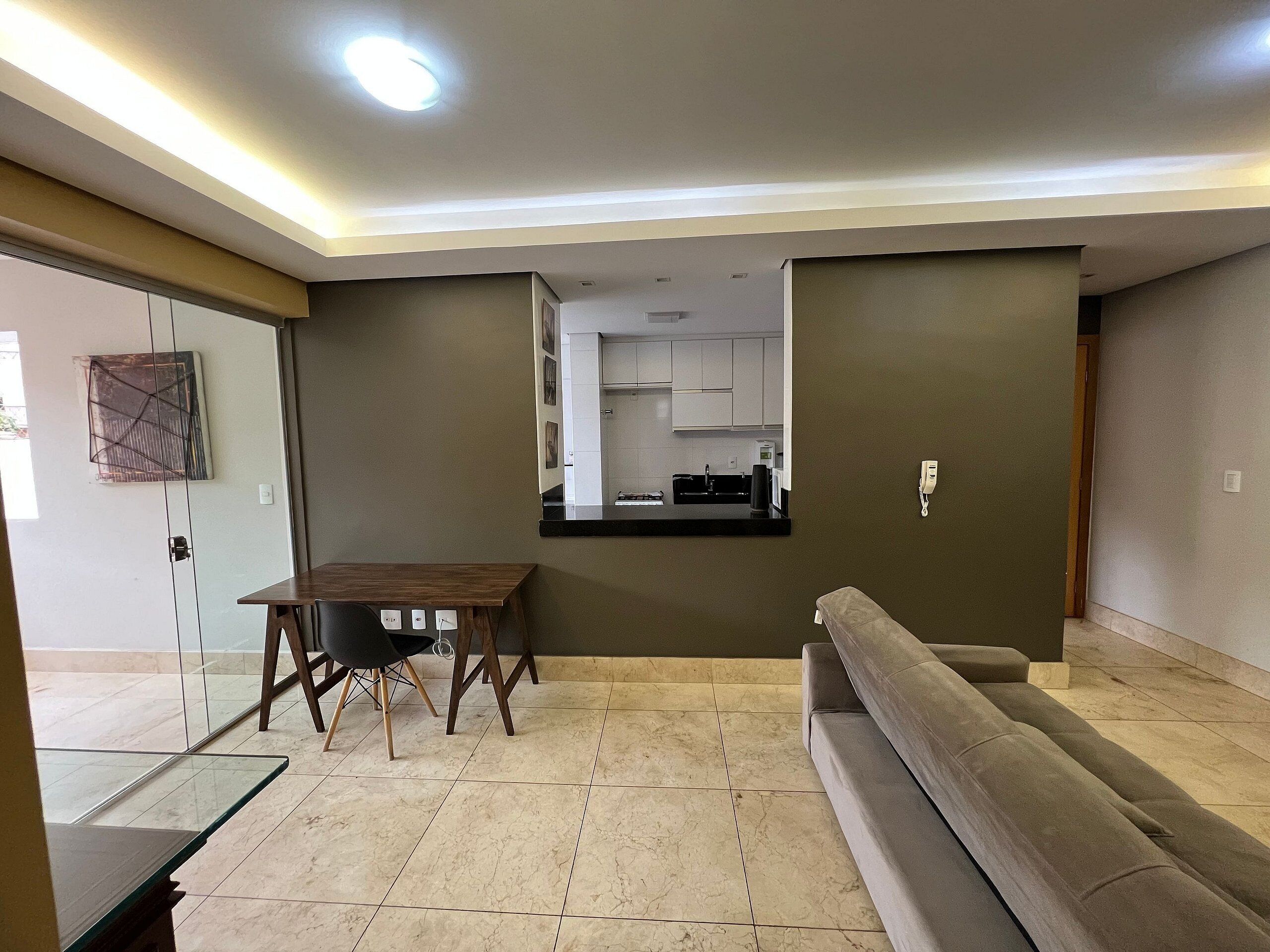 A modern living room with a sofa, a dining table, and a kitchen area visible through an open door.