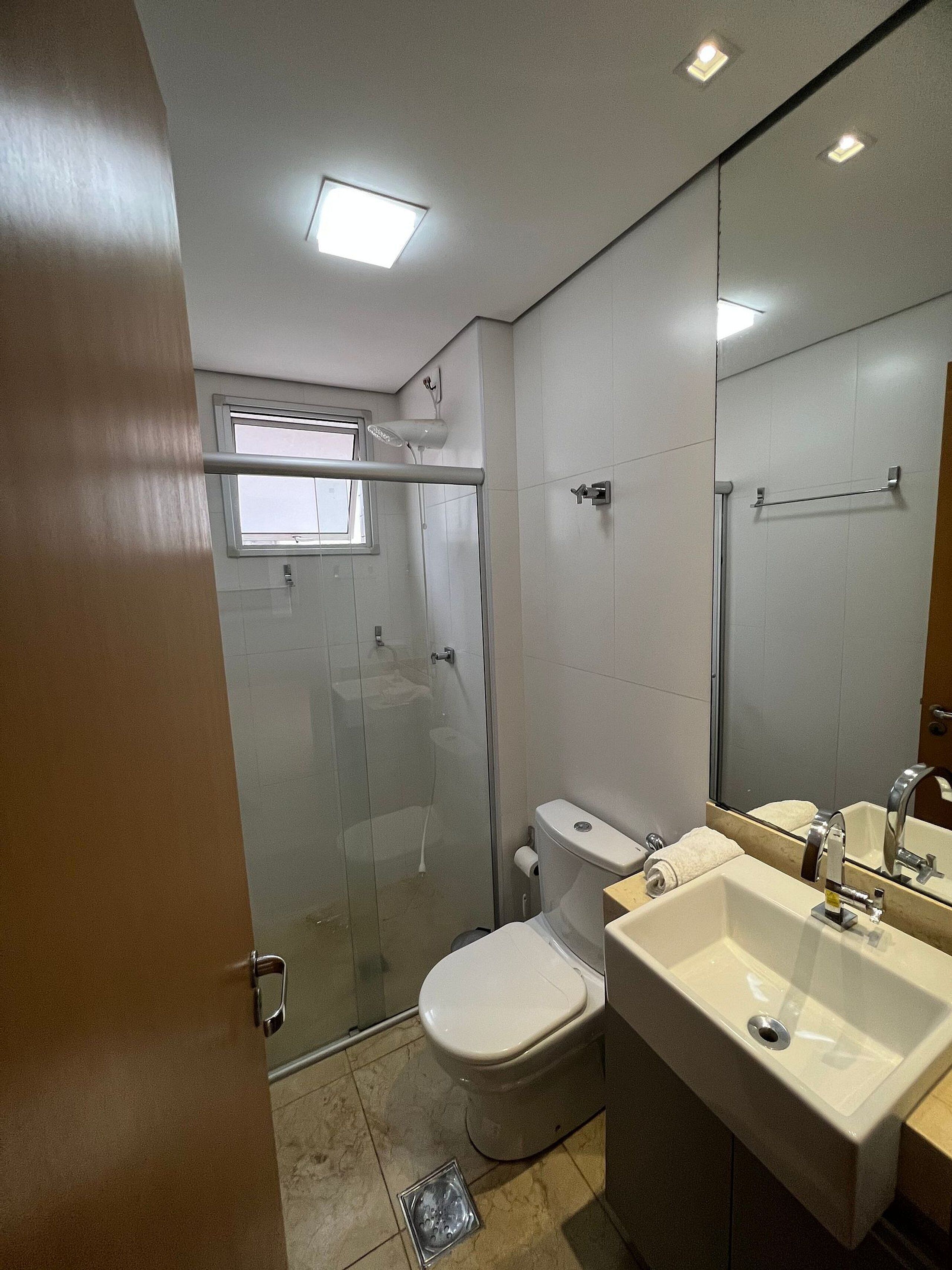 A bathroom with a glass-enclosed shower, a toilet, a sink, and a mirror.