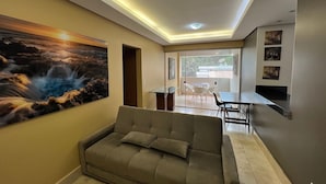 Una sala de estar con un sofá, un cuadro, un comedor con sillas y una mesa, e iluminación empotrada en el techo.