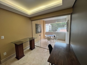 Quarto com divisória de vidro, uma mesa de madeira, escrivaninha com tampo de vidro e um quadro na parede.