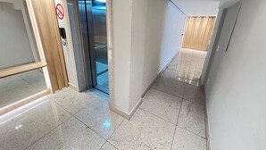 Un pasillo moderno con suelo de baldosas brillantes, un cartel de prohibición de fumar y un ascensor de vidrio.