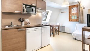 A compact kitchen with a microwave, dishwasher, and a dining area with a table and chairs. - Cosy Alpine Studio for Romantic Getaway (Gresse-en-Vercors)