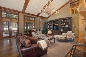 Ein großzügiges Wohnzimmer mit Ledersofa, gemusterten Sessel, Kamin und einer großen Holzbibliothek.