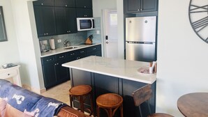 A compact kitchen with dark cabinets, a microwave, a refrigerator, a coffee maker, and a small island with stools. - NEW LISTING: Stylish, scenic & renovated condo steps from Caribbean in Red Hook! (St Thomas)