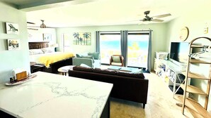 A living room with a sofa, a coffee table, a TV, and a balcony with a view. - NEW LISTING: Stylish, scenic & renovated condo steps from Caribbean in Red Hook! (St Thomas)