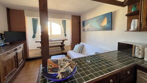 A cozy kitchen with a tiled countertop, a dining area with a bench, a white sofa, and a painting of a sailboat on the wall. - direct seaside rental (Cerbère)