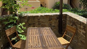 A wooden table and chairs under a pergola, with a stone wall and greenery in the background. - direct seaside rental (Cerbère)
