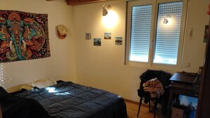 Una camera da letto con un letto, una scrivania, una sedia, un arazzo e una finestra con persiane.