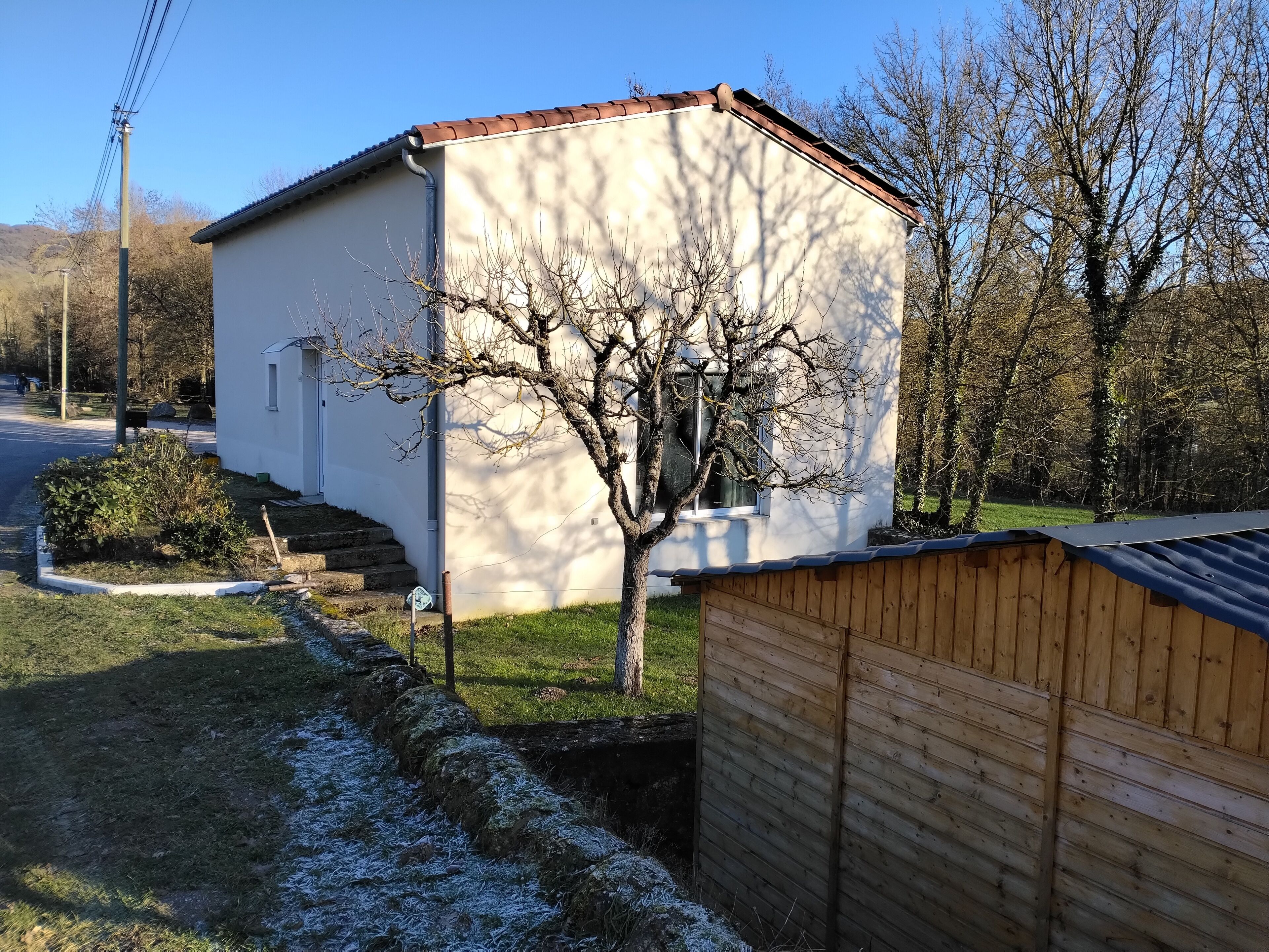 Ein kleines, einstöckiges Gebäude mit schrägem Dach, einem Fenster und einem Baum davor.