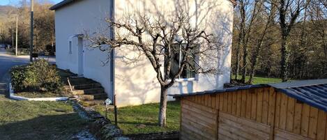 Ein kleines, einstöckiges Gebäude mit schrägem Dach, einem Fenster und einem Baum davor.