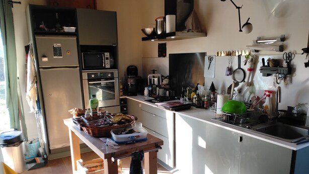 Cucina attrezzata con frigorifero, microonde, forno e lavello. Si nota un tavolo con un cesto e un espositore per piatti.