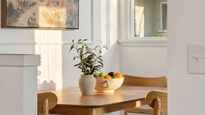 A dining area with a table, chairs, a bowl of fruit, a potted plant, and a painting on the wall. - 10 MIN to Disney - Family Dream Home-King Bed! (Fullerton)