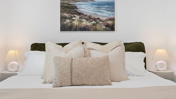 A bedroom with a bed, pillows, a nightstand, a lamp, and a painting of a coastal landscape. - 10 MIN to Disney - Family Dream Home-King Bed! (Fullerton)