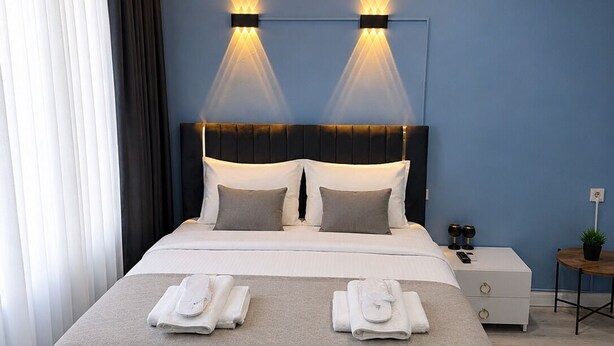 Habitación de hotel moderna con una cama grande, dos mesitas de noche y una pequeña mesa con una planta.