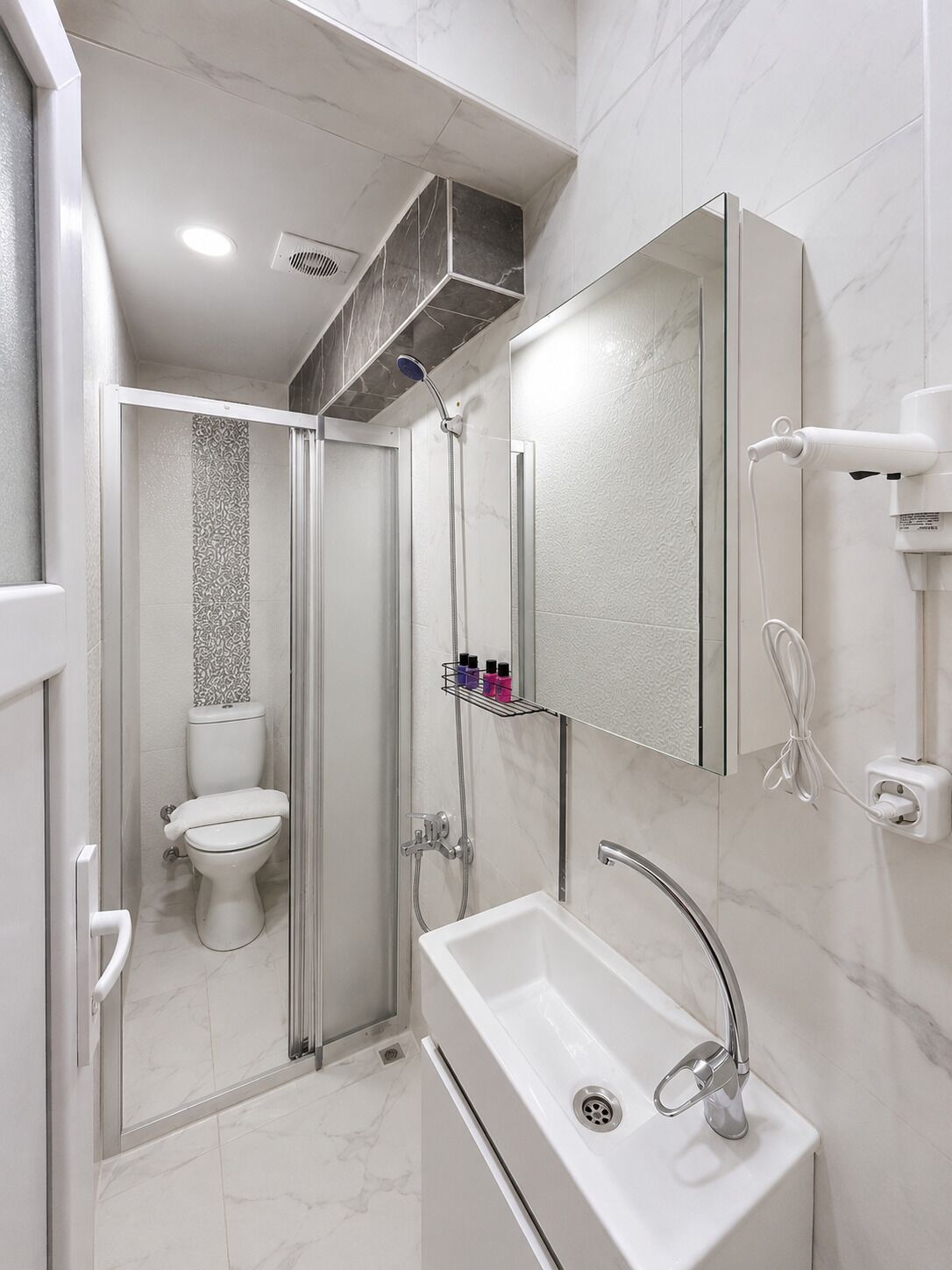 Ein modernes Badezimmer mit Glasdusche, Toilette, Waschbecken mit Spiegel und Handtuchhalter.