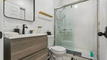 Een moderne badkamer met een douchecabine van glas, een wit toilet en een wastafel met spiegel.