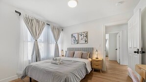 A bedroom with a bed, bedside tables, a nightstand, a door, and a hallway. - Hayward 5BR Cozy Spacious House, AC/Free Parking (Hayward)
