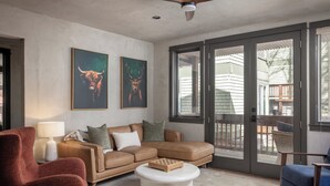 A living room with a brown sectional sofa, a red armchair, a white coffee table, and two framed animal paintings on the wall. - Stylish Renovated Telluride 2BR Condo – Walk to Ski, Town, Shops & Restaurants, Sleeps 6 (Telluride)